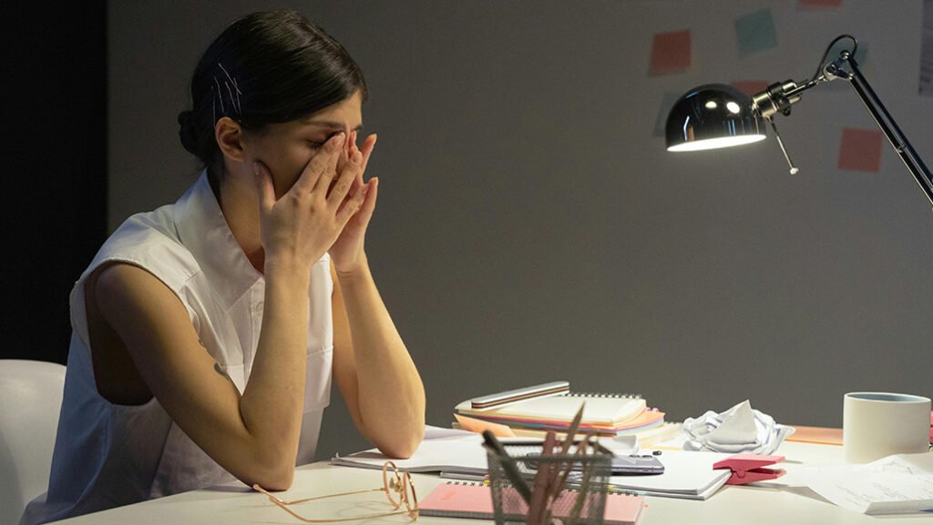 Women at desk hands over face looking overwhelmed