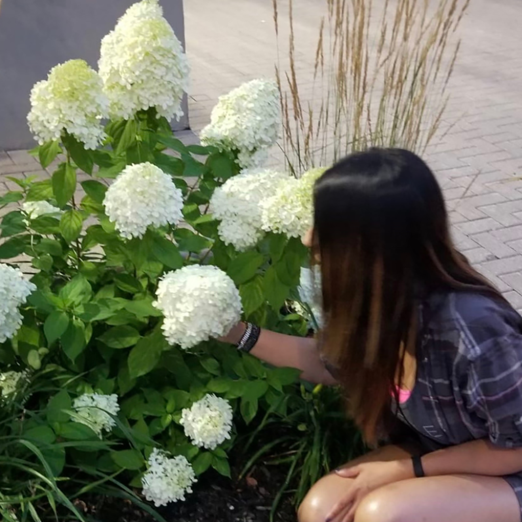 Nadia infront of flowers, smelling a large white one, practicing mindfulness