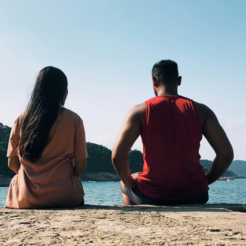 two people sitting on the beach looking aheard